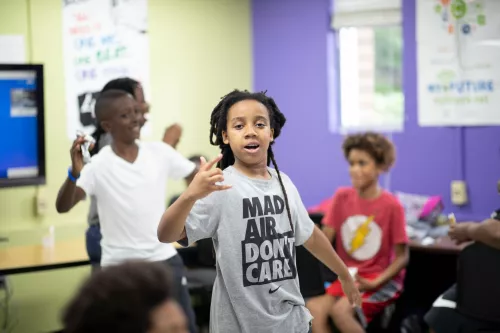 Youth speaking with arm raised with other youth behind. 