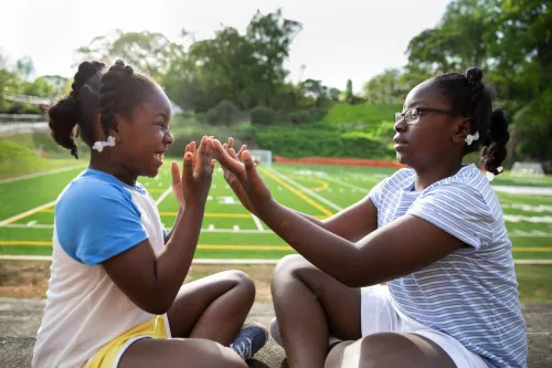 Youth sitting across from each other, holding hands up to each other.